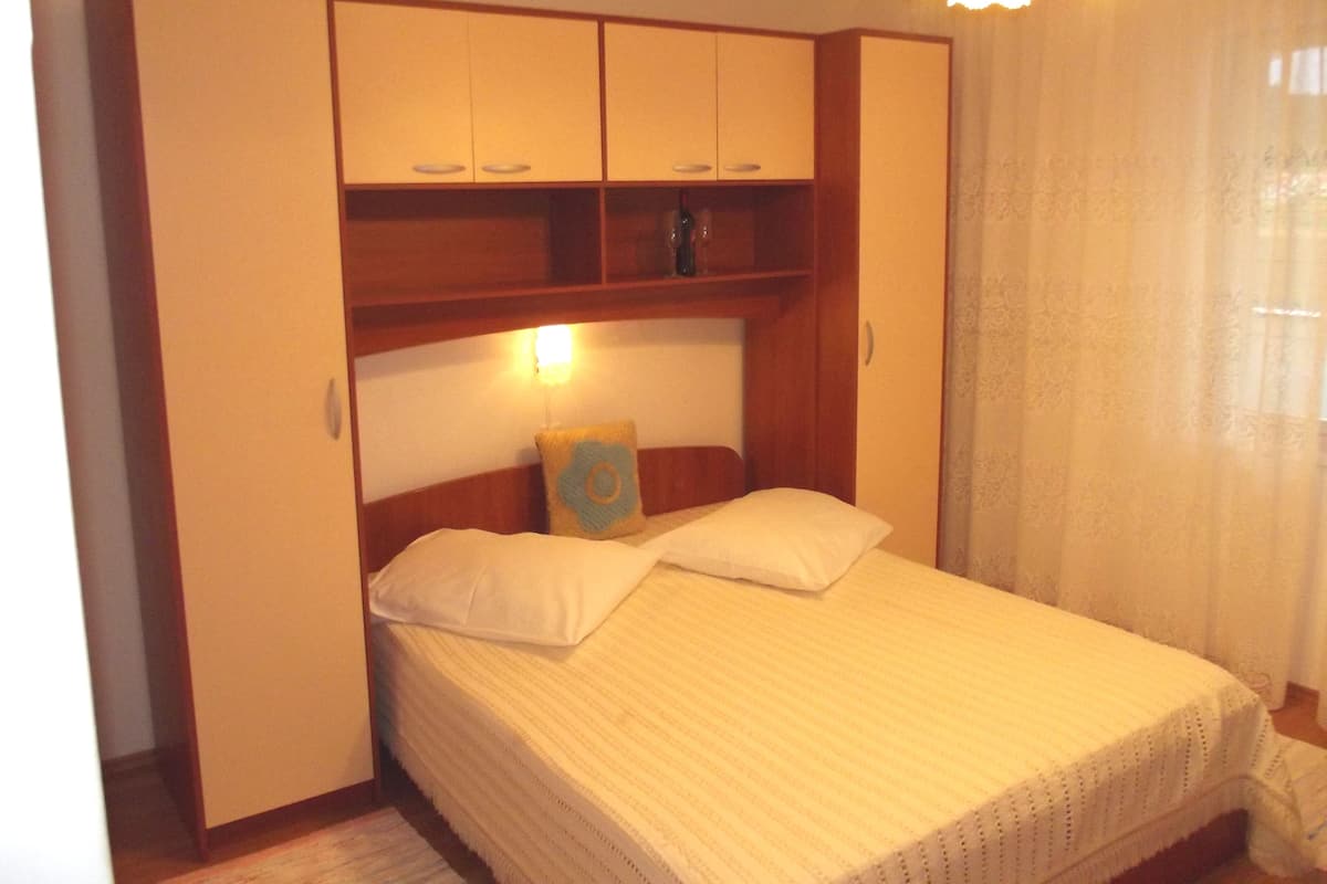 A bedroom with a bed, a nightstand, a wardrobe, and a window with curtains.