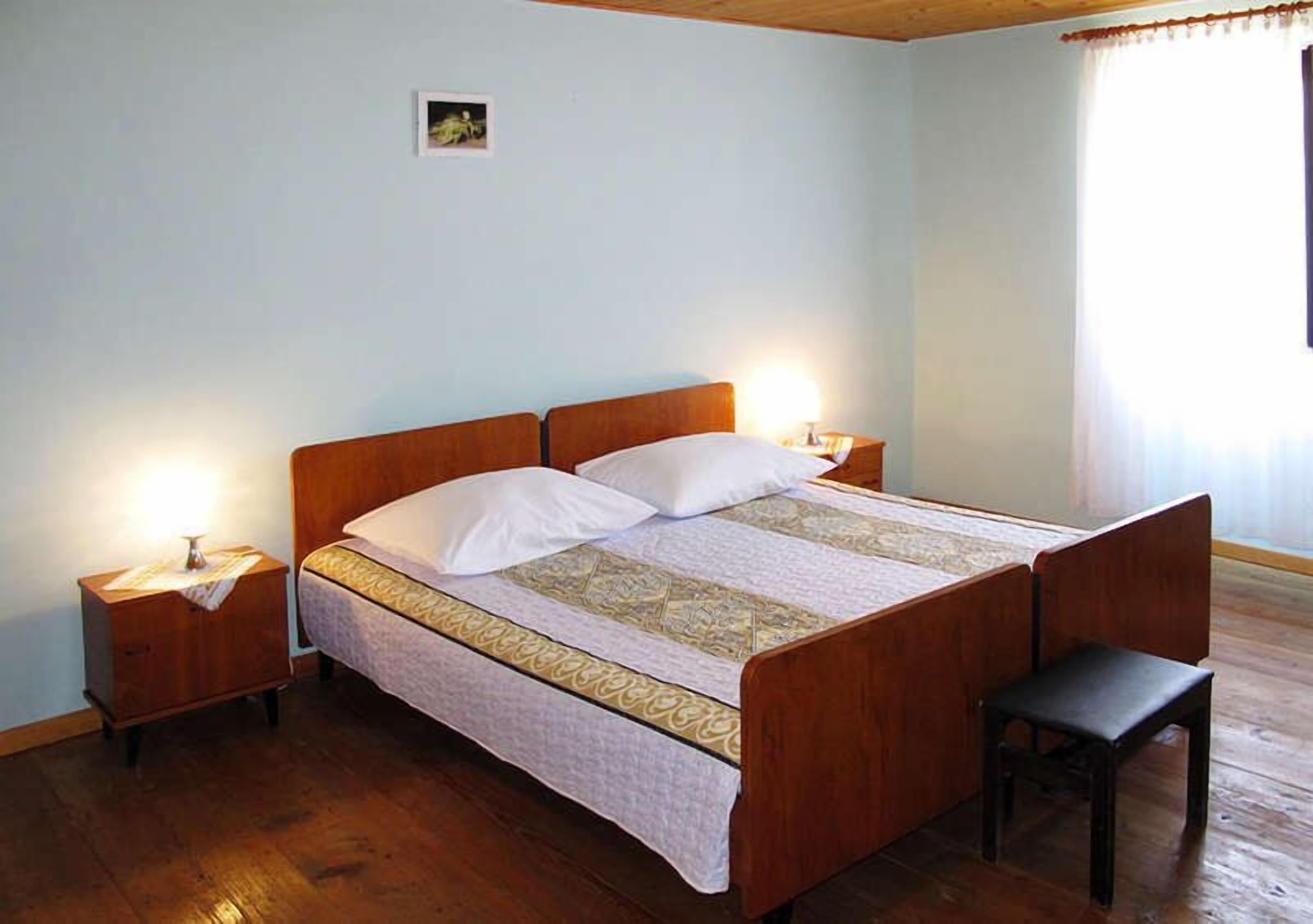 A neatly made bed with a wooden headboard, two bedside tables with lamps, and a small bench.