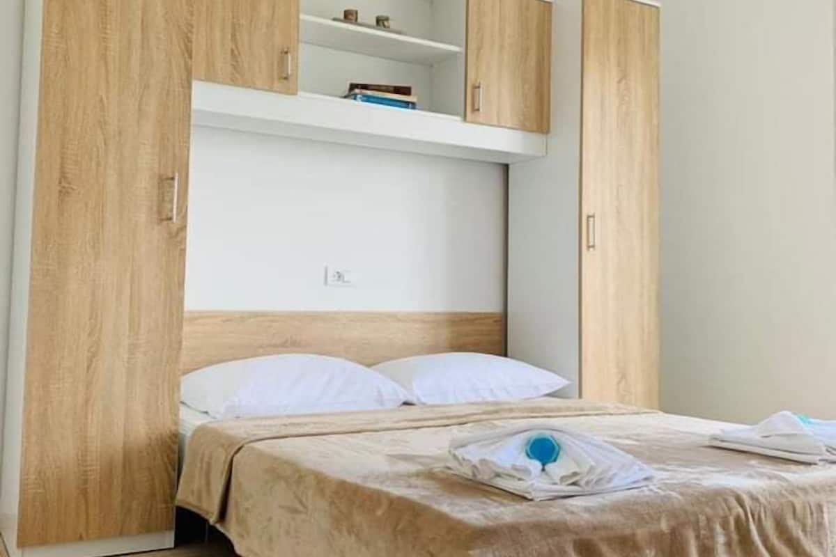 A bedroom with a bed, wooden wardrobe, and a shelf unit.