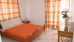 Un dormitorio con cama de madera, ropa de cama naranja, una mesita de noche y un florero con flores.