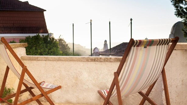 Two wooden lounge chairs with striped cushions on a balcony with a view of a building and a church in the background.