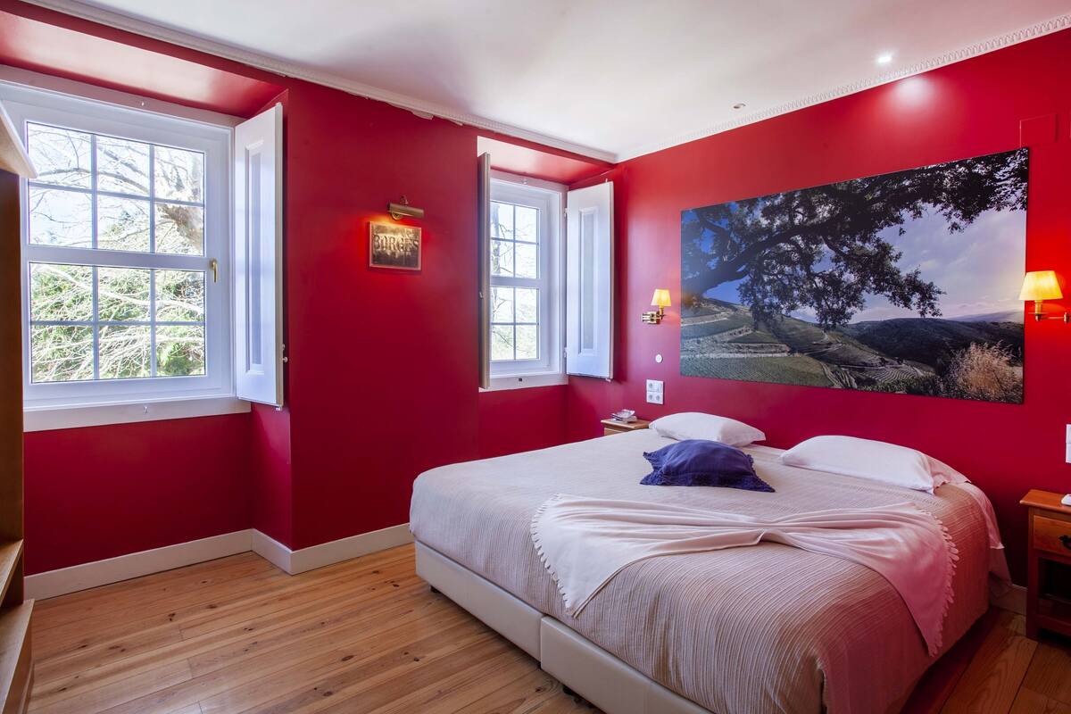 Slaapkamer met rode wanden, een groot bed, twee ramen en een landschap schilderij.