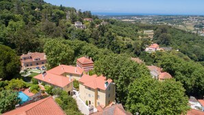 A hillside property with multiple buildings, including a large house with a swimming pool and a smaller building with a red roof.