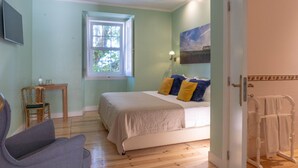 A bedroom with a bed, a chair, a window, a painting, and a door.