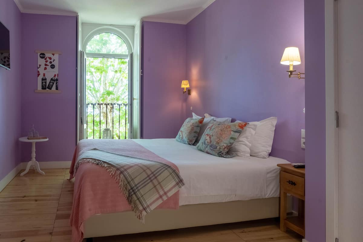 Een slaapkamer met een bed, nachtkastje, lamp, raam en deur.