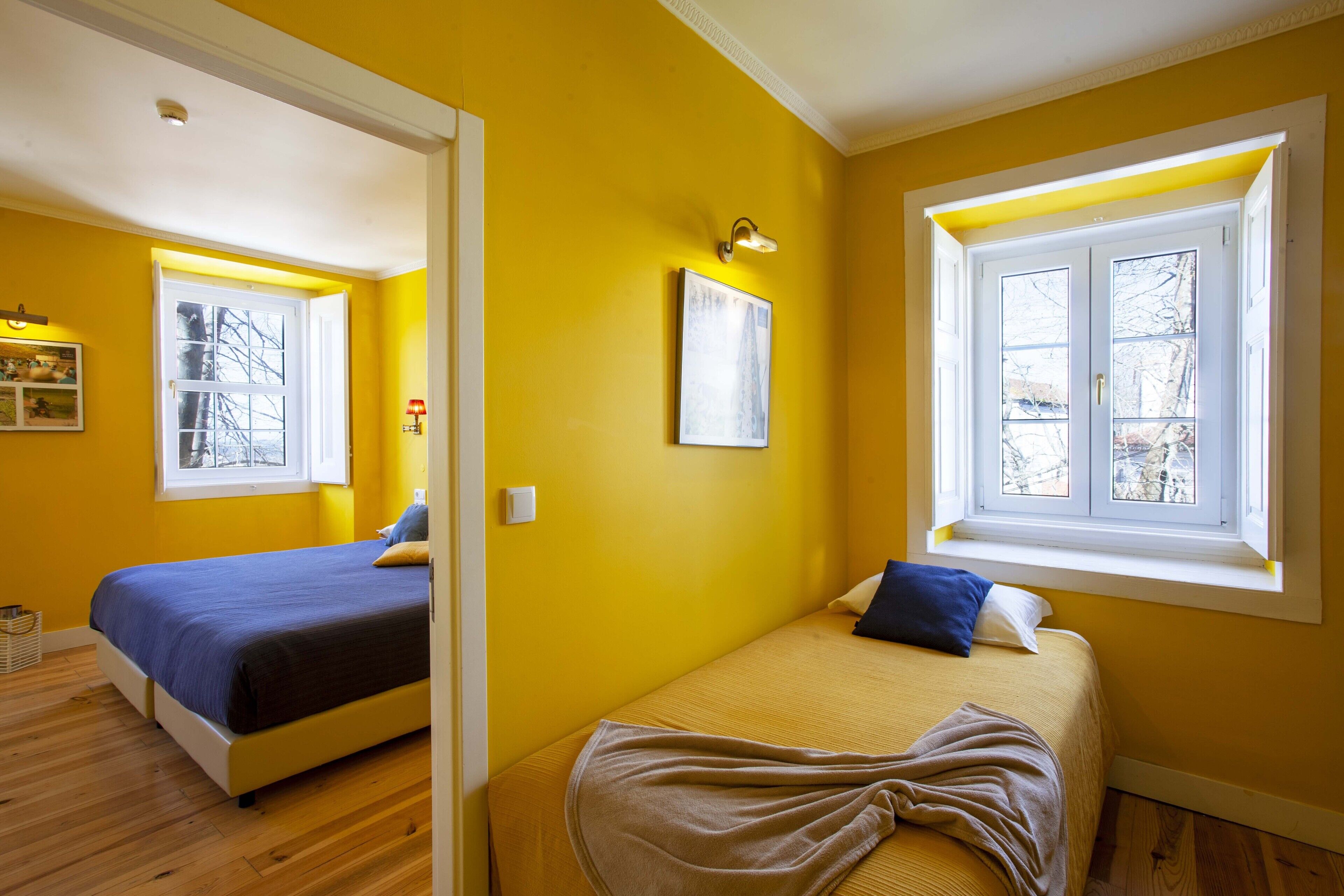 A room with two beds, a window, and a mirror reflecting another room.