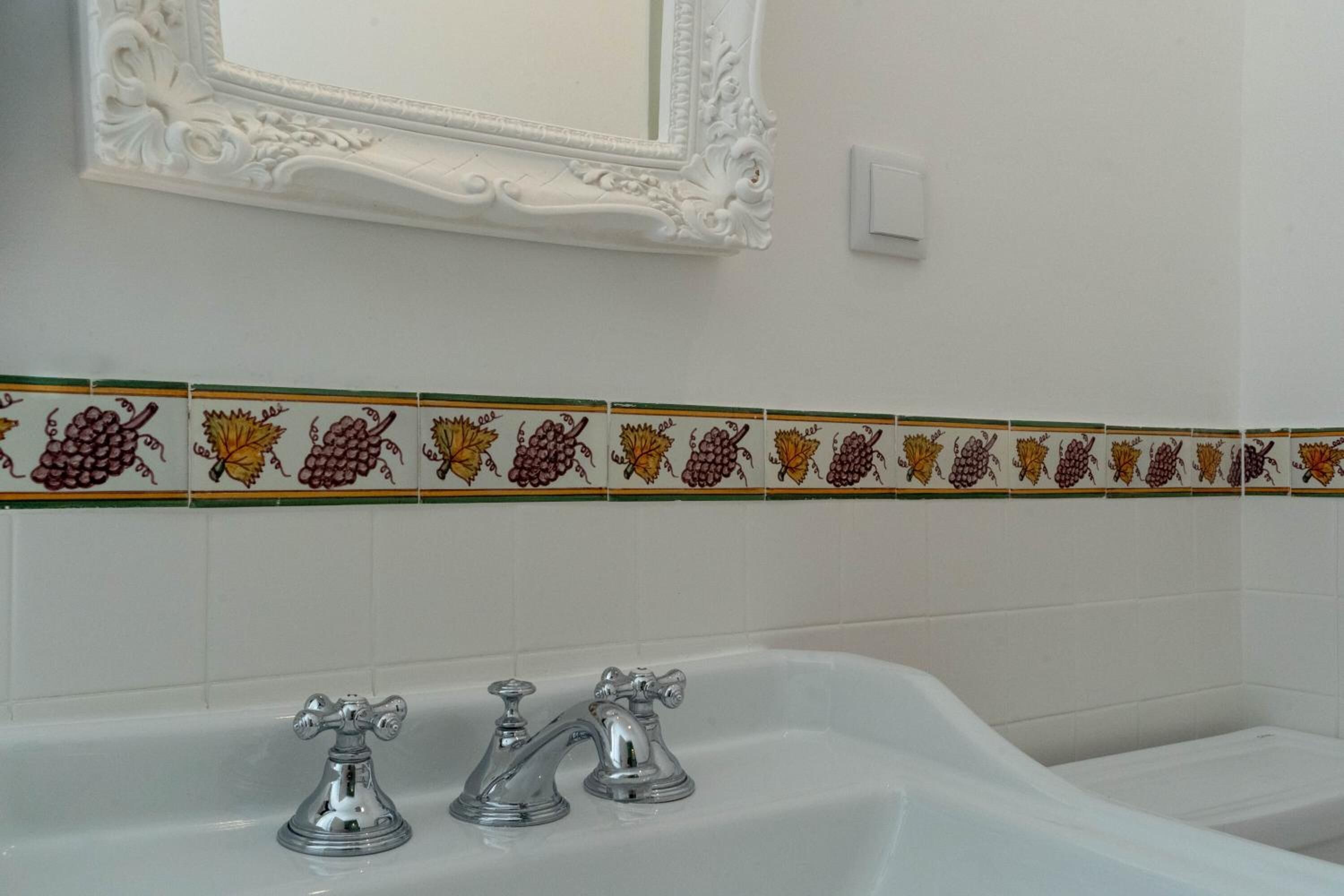 A bathroom with a white bathtub, two faucets, and a decorative tile border with fruit designs.