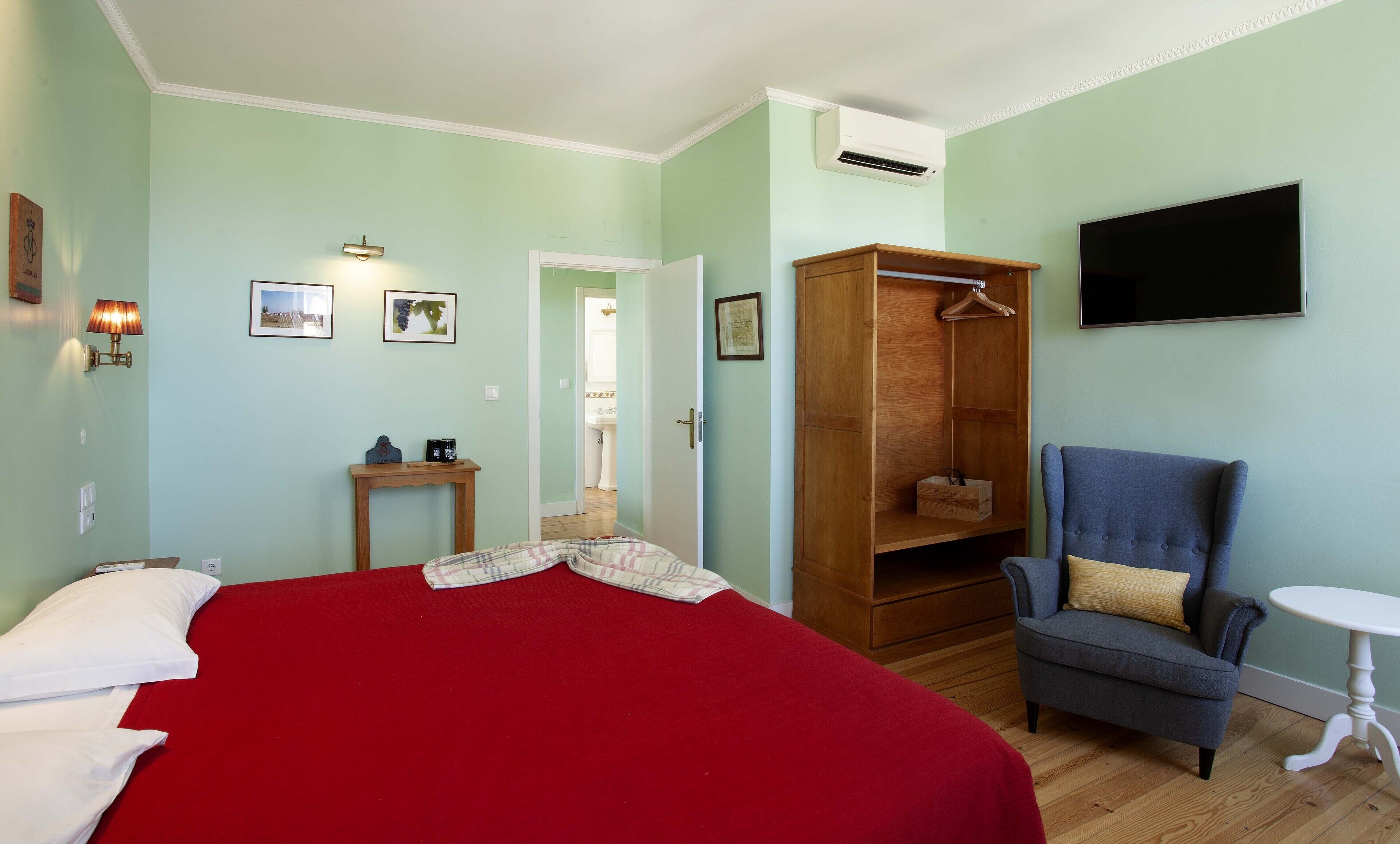A bedroom with a bed, a wardrobe, a chair, a table, and a TV.
