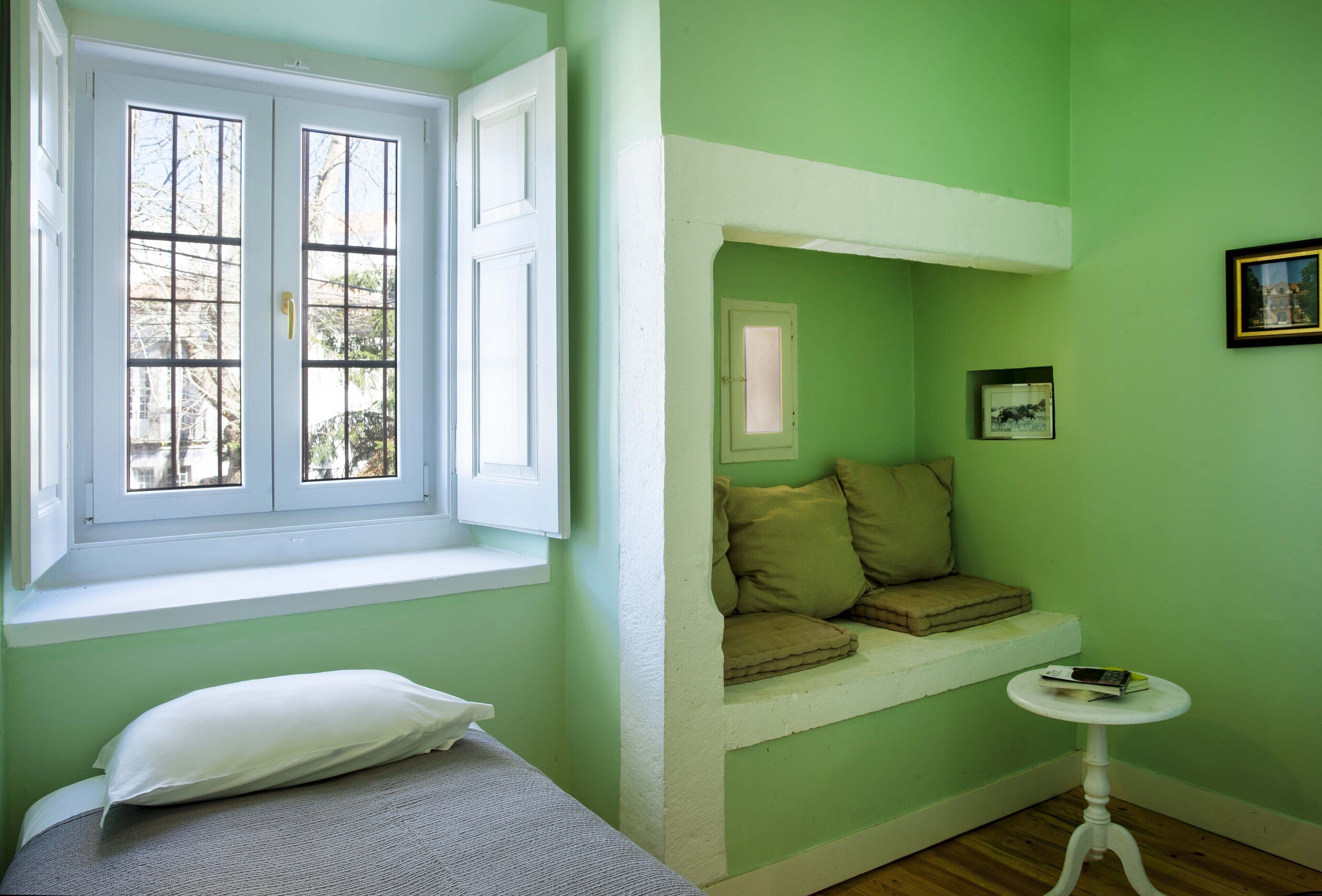 A room with a bed, a window, a small table, and a built-in bench with cushions.
