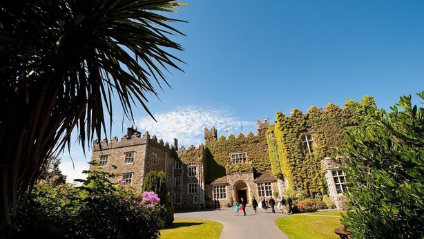 A historic stone building with ivy-covered walls, a central archway, and a paved pathway leading to the entrance. - Waterford Castle Lodges (Waterford)