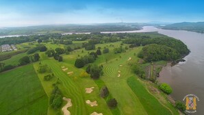 An aerial view of a golf course with multiple greens, sand bunkers, and a river in the background. - Waterford Castle Lodges (Waterford)