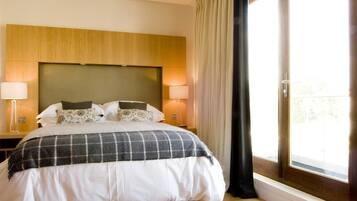 A hotel room with a large bed, two bedside lamps, a wooden headboard, and a view through a large window.