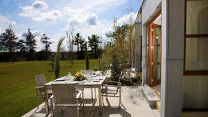 An outdoor dining area with a table set for four, surrounded by chairs, near a modern building with large windows. - Waterford Castle Lodges (Waterford)