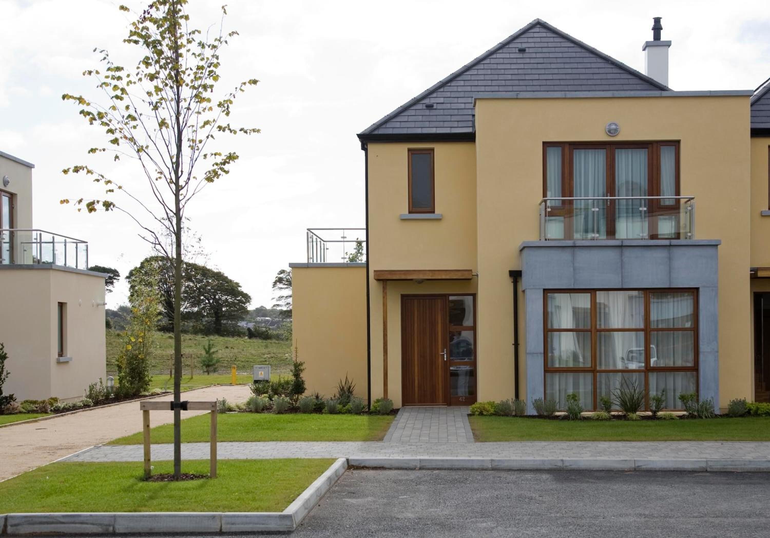 A modern two-story house with a flat roof, a balcony, and a well-maintained lawn.