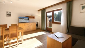 A modern living room with a wooden dining table, chairs, a sofa, and a TV on a wooden cabinet.