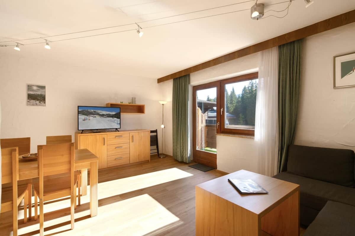 A modern living room with a wooden dining table, chairs, a sofa, and a TV on a wooden cabinet.