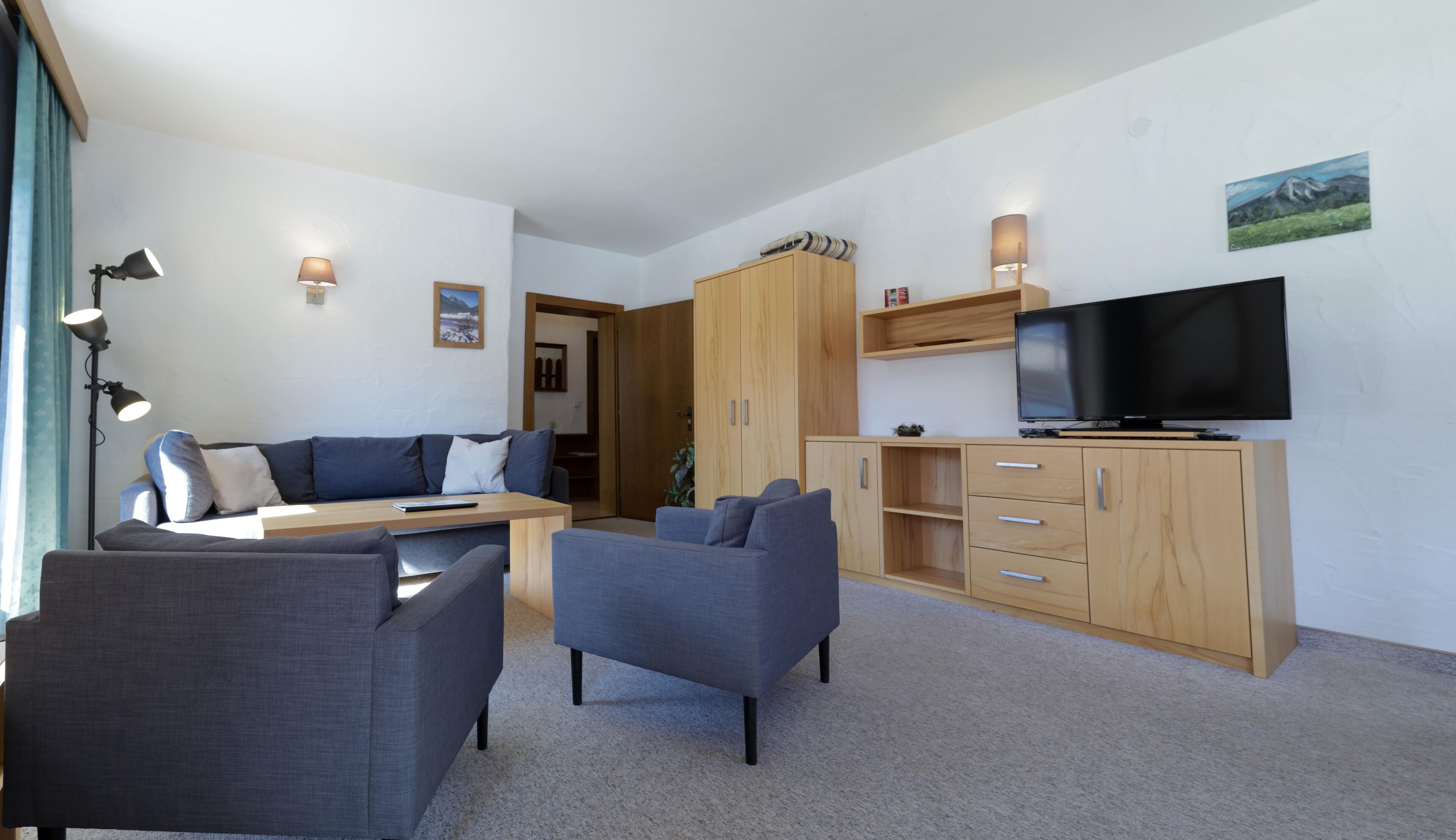 A modern living room with a sofa, two armchairs, a coffee table, a TV, and wooden cabinets.