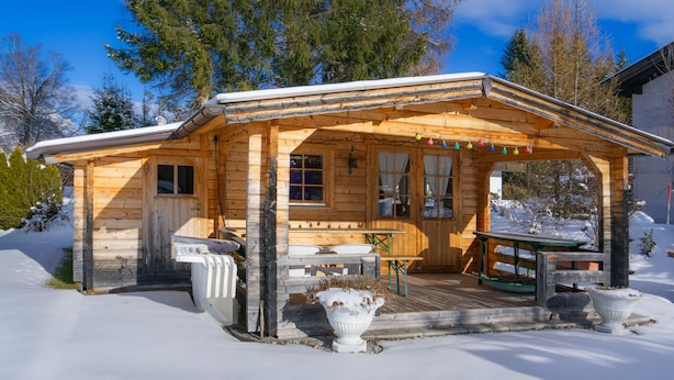 A wooden cabin with a porch, a wooden table, and a bench.
