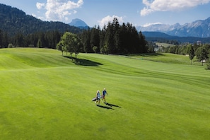Un parcours de golf avec un ciel dégagé, des arbres et des montagnes à l’horizon.