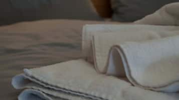 Ein ordentlich bezogenes Bett mit einem gefalteten Handtuch, zwei Kissen und einem Kopfteil mit Wandleuchten.