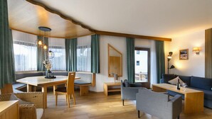 A modern living room with a wooden dining table, comfortable seating, and a large window with curtains.