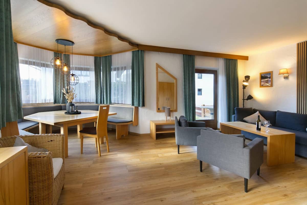 A modern living room with a wooden dining table, comfortable seating, and a large window with curtains.