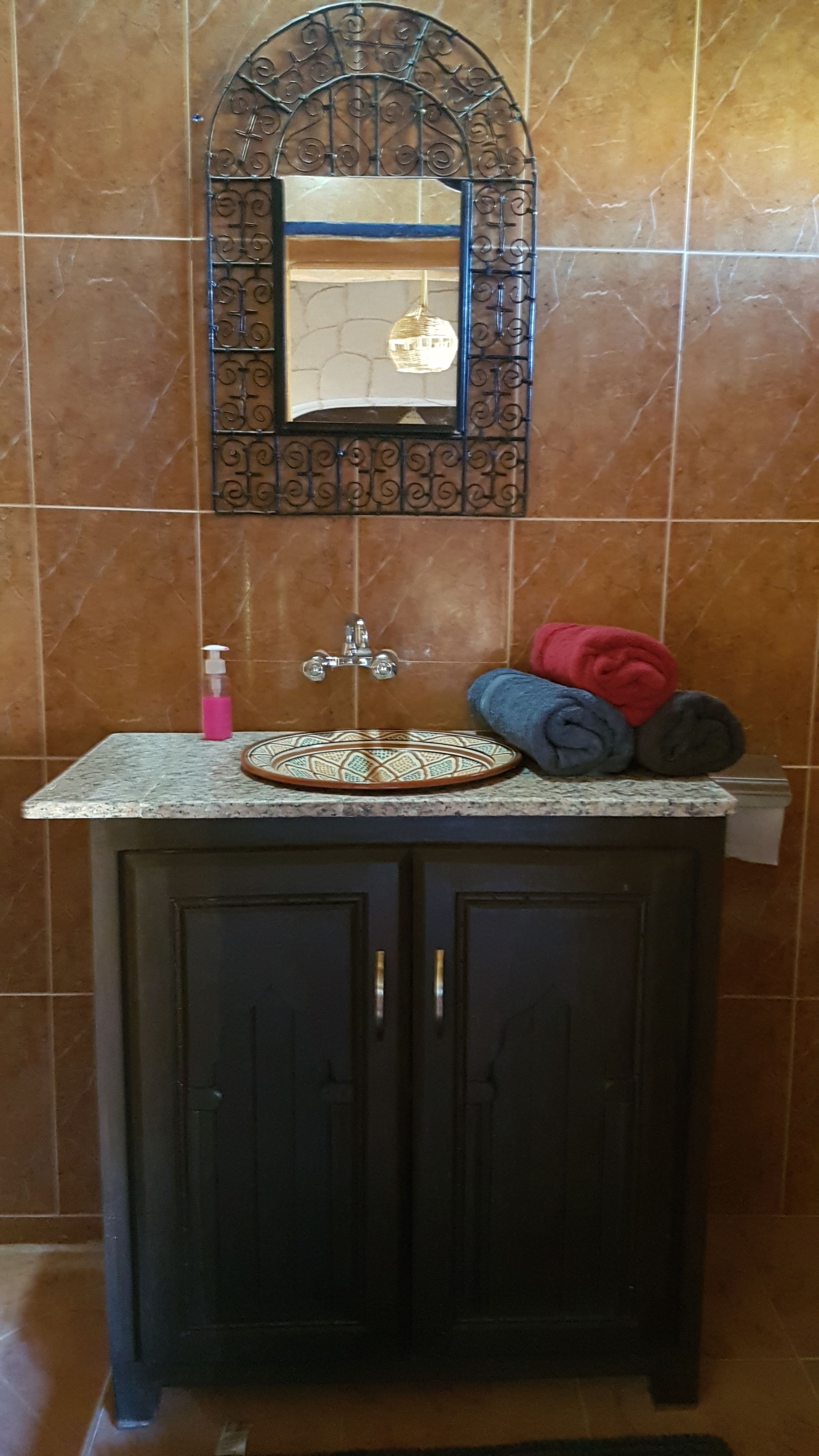 A bathroom with a dark wooden cabinet, a sink with a decorative mirror, and a towel rack with towels.