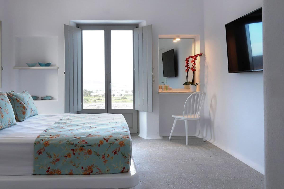 Un dormitorio con cama, escritorio, silla, televisor y ventana con vistas.