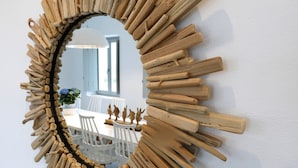 Ein Spiegel mit sonnenförmigem Holzrahmen, der einen Essbereich mit weißen Stühlen und einem Tisch zeigt.