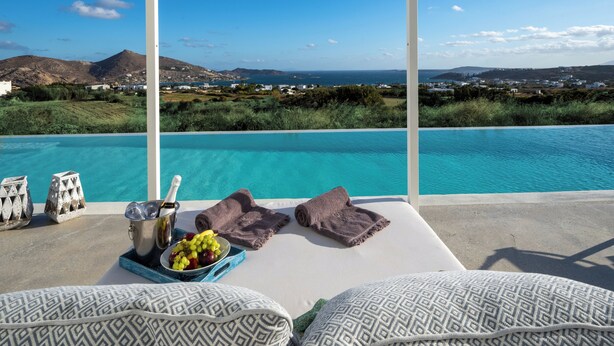 Eine Poolliege mit freiem Blick auf das Meer und die Hügel, eine Champagnerflasche und eine Obstschale.