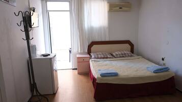 Un dormitorio con cama, mesita de noche, escritorio pequeño, radiador y ventana con cortinas.