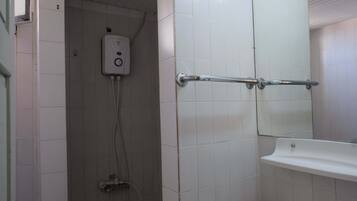 Une salle de bain avec des carreaux blancs, une douchette à main, une barre d’appui et un lavabo.