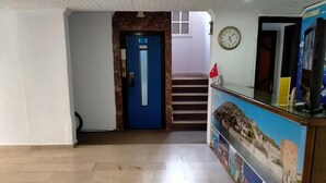 A hotel lobby with a blue door, a staircase, and a reception desk with a clock. - Hisar Otel (Alanya)