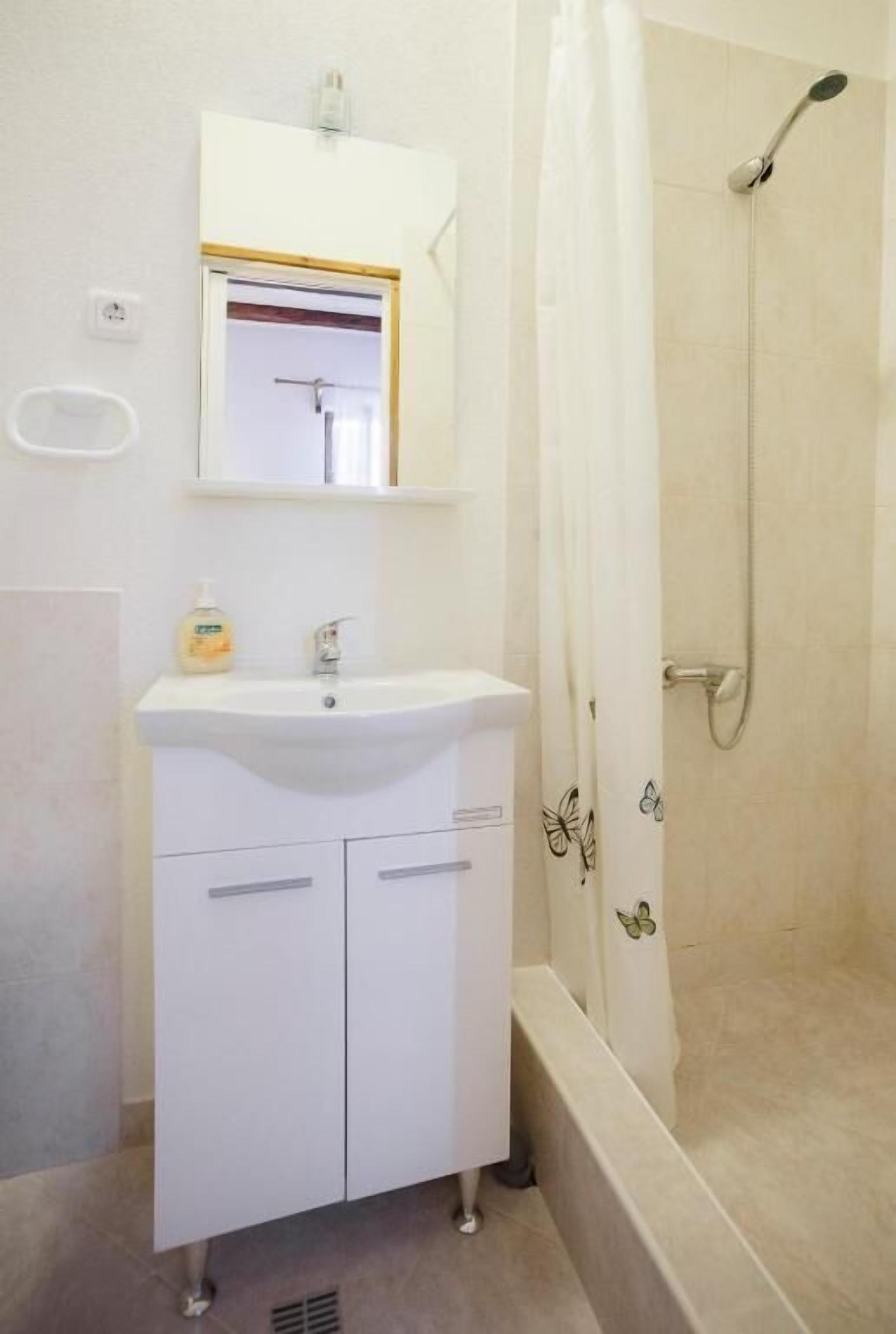 A bathroom with a white sink, mirror, and shower.