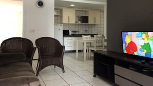 A living room with a sofa, two wicker chairs, a TV, and a kitchen in the background. - Altavista Apartments (Fortaleza)