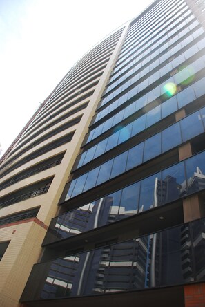 Um edifício alto e moderno com fachada de vidro refletivo e várias varandas.