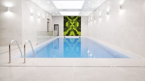 Una piscina interior con agua cristalina, rodeada de paredes blancas y una pared estampada de color verde al fondo.
