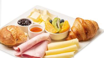 Une assiette garnie de jambon, de fromage, de croissants et de fruits.