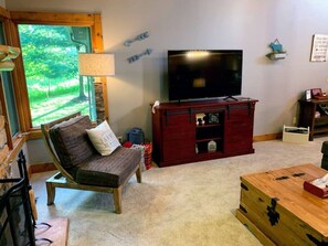 A cozy living room with a wooden bench, a TV on a red cabinet, and a view of greenery outside.