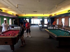 A pool hall with multiple pool tables, a ceiling with recessed lighting, and a view of the outdoors through large windows.