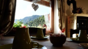 Una mesa de comedor con vajilla verde, un adorno con forma de corazón y vistas a un paisaje montañoso a través de una ventana.