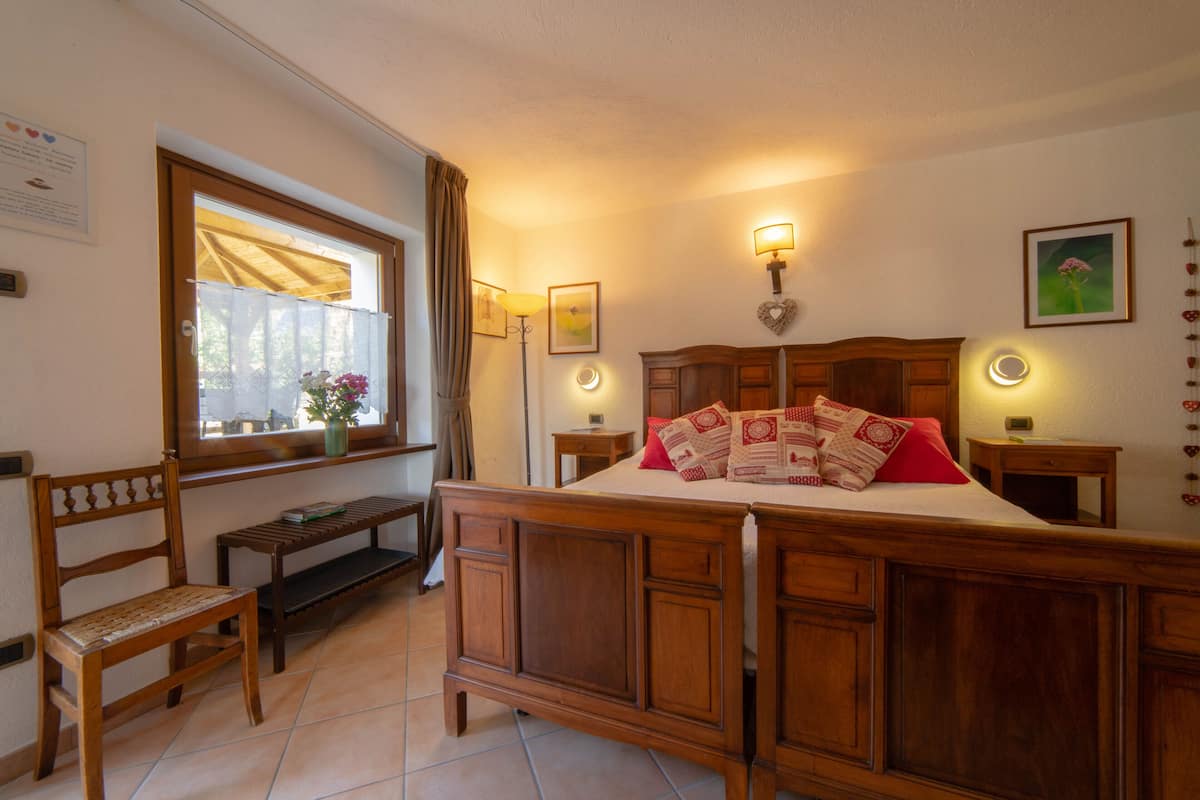 A bedroom with a wooden bed, a bench, a window with curtains, and wall-mounted lamps.
