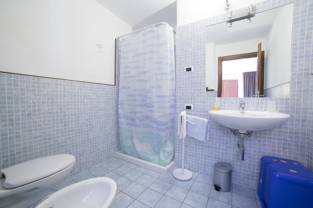 Et badeværelse med bruser, toilet, håndvask og et blå skab.