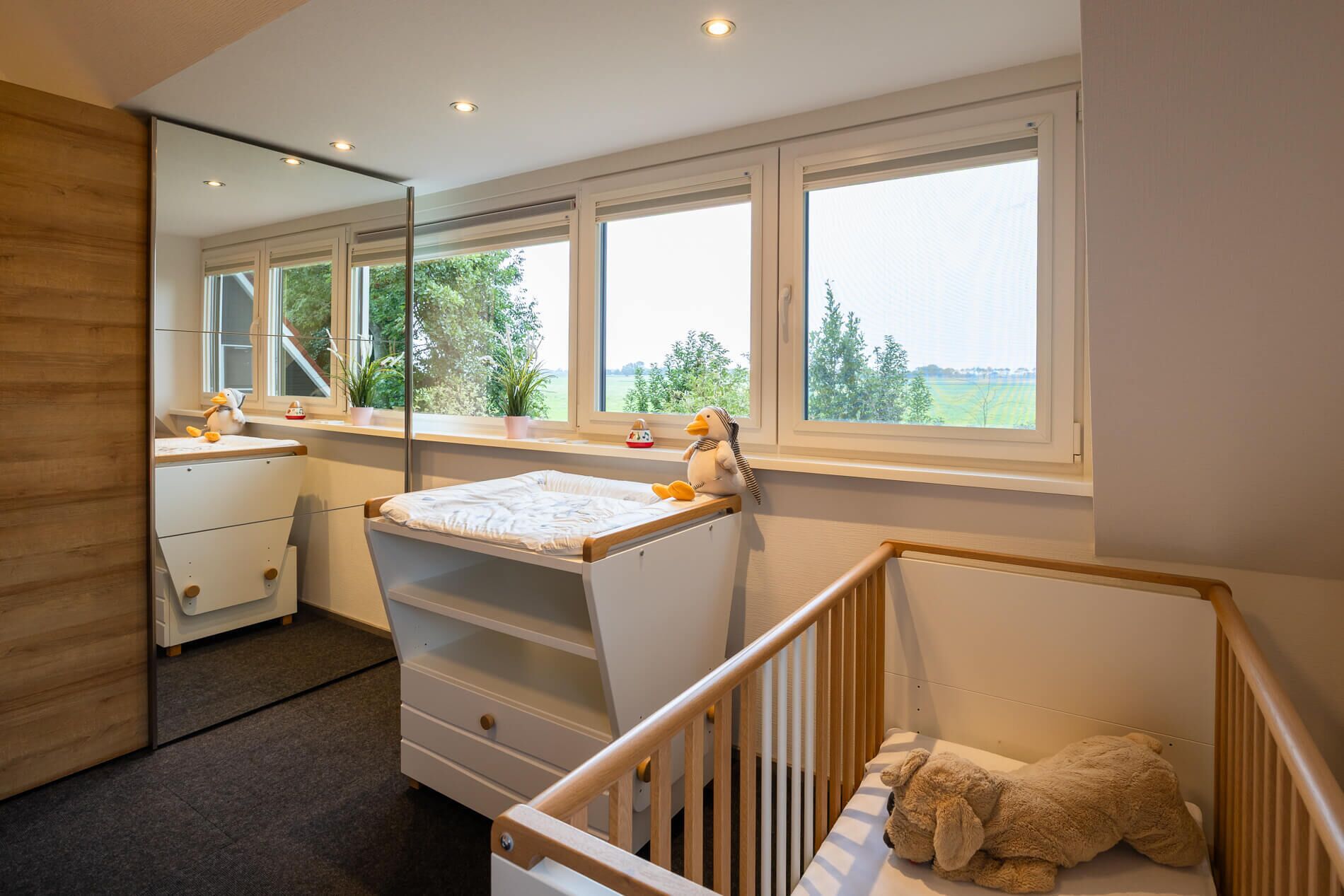 A baby room with a crib, changing table, and a large window with a view of greenery.