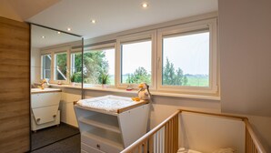 A baby room with a crib, changing table, and a large window with a view of greenery. - Detached vacation home with its own beach cabana, 2-gigabit internet, and pool (Sint Maarten)