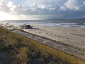 Une plage avec un bâtiment, une promenade en bord de mer et des dunes herbeuses.