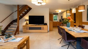 A modern living room with a wooden staircase, a flat-screen TV, a dining area with a wooden table and chairs, and pendant lighting. - Detached vacation home with its own beach cabana, 2-gigabit internet, and pool (Sint Maarten)