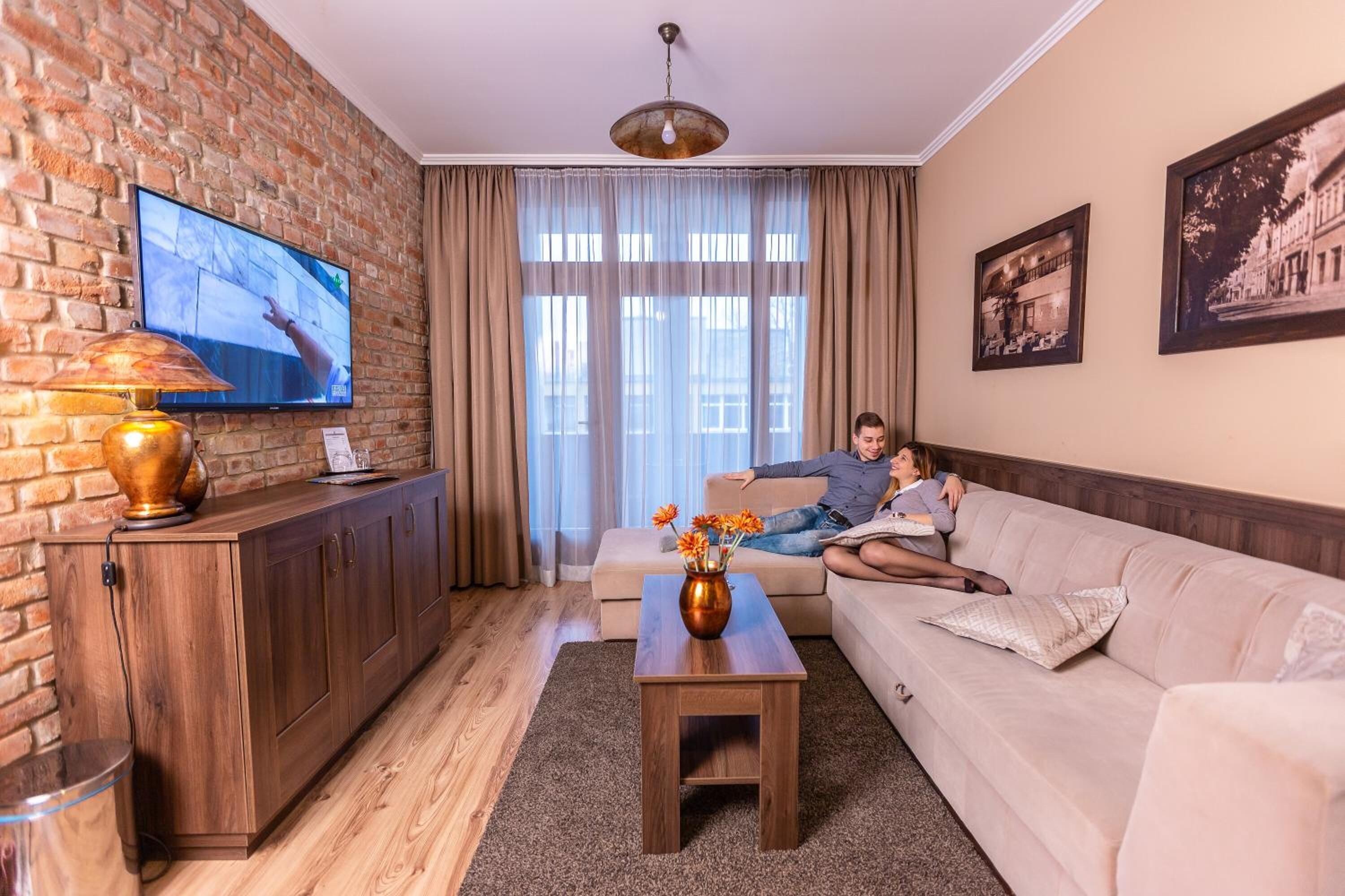 A living room with a brick wall, a TV, a sofa, a coffee table, and a vase with flowers.