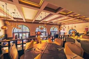 Un interior de restaurante con techos altos, ventanas arqueadas, lámparas colgantes y una larga mesa de comedor.
