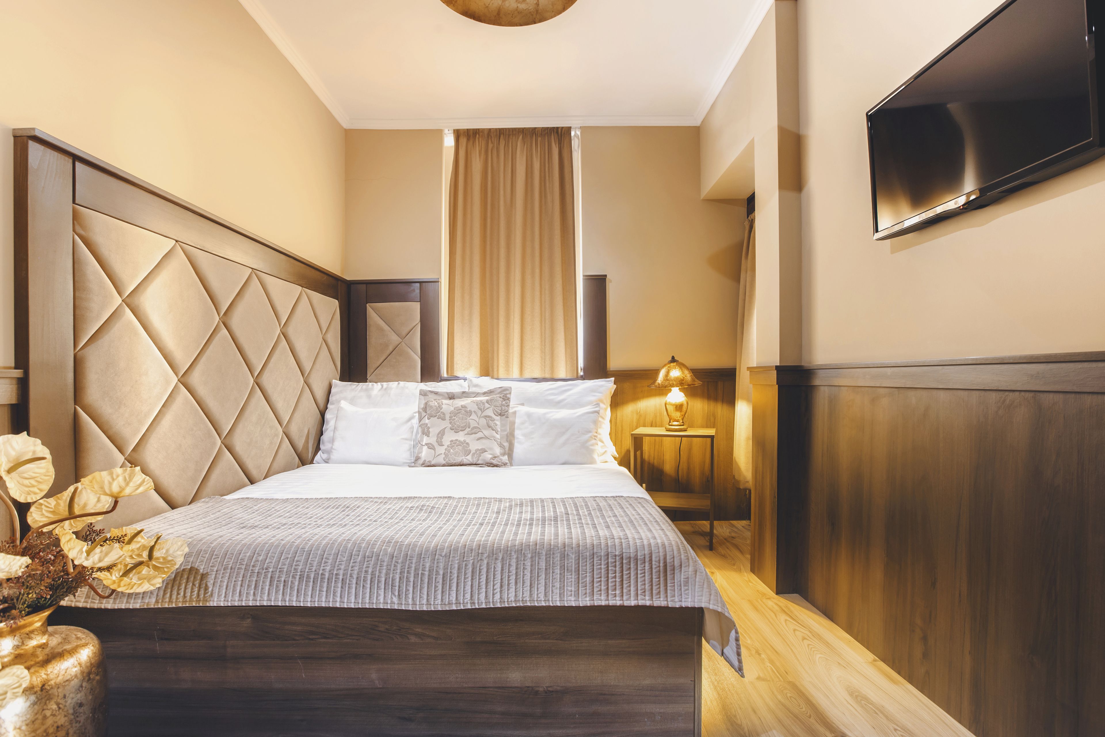 Una habitación de hotel moderna con una cama grande, un televisor de pantalla plana montado en la pared y una mesita de noche con lámpara.